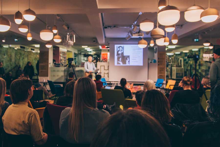 Yleisöä hämärästi valaistussa tilassa.